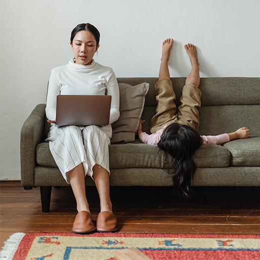 family on couch with mother with laptop and young daughter sitting upside down